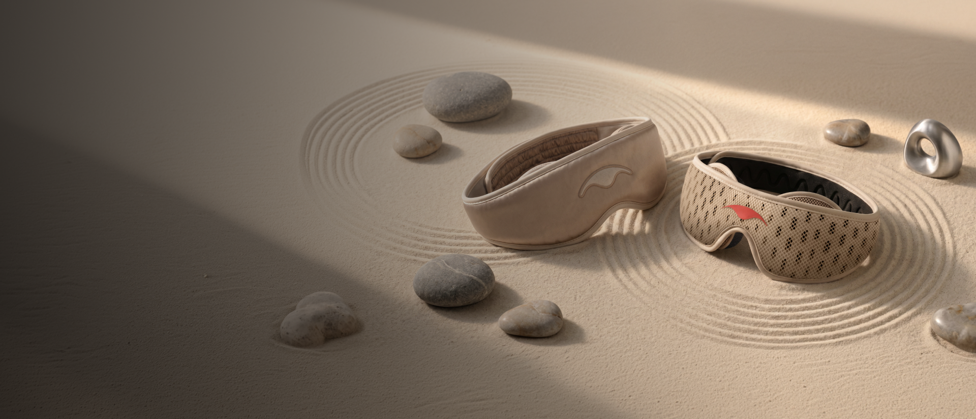 Tranquil Taupe variants of Manta SILK and PRO Sleep Masks on a sandy surface with pebbles.